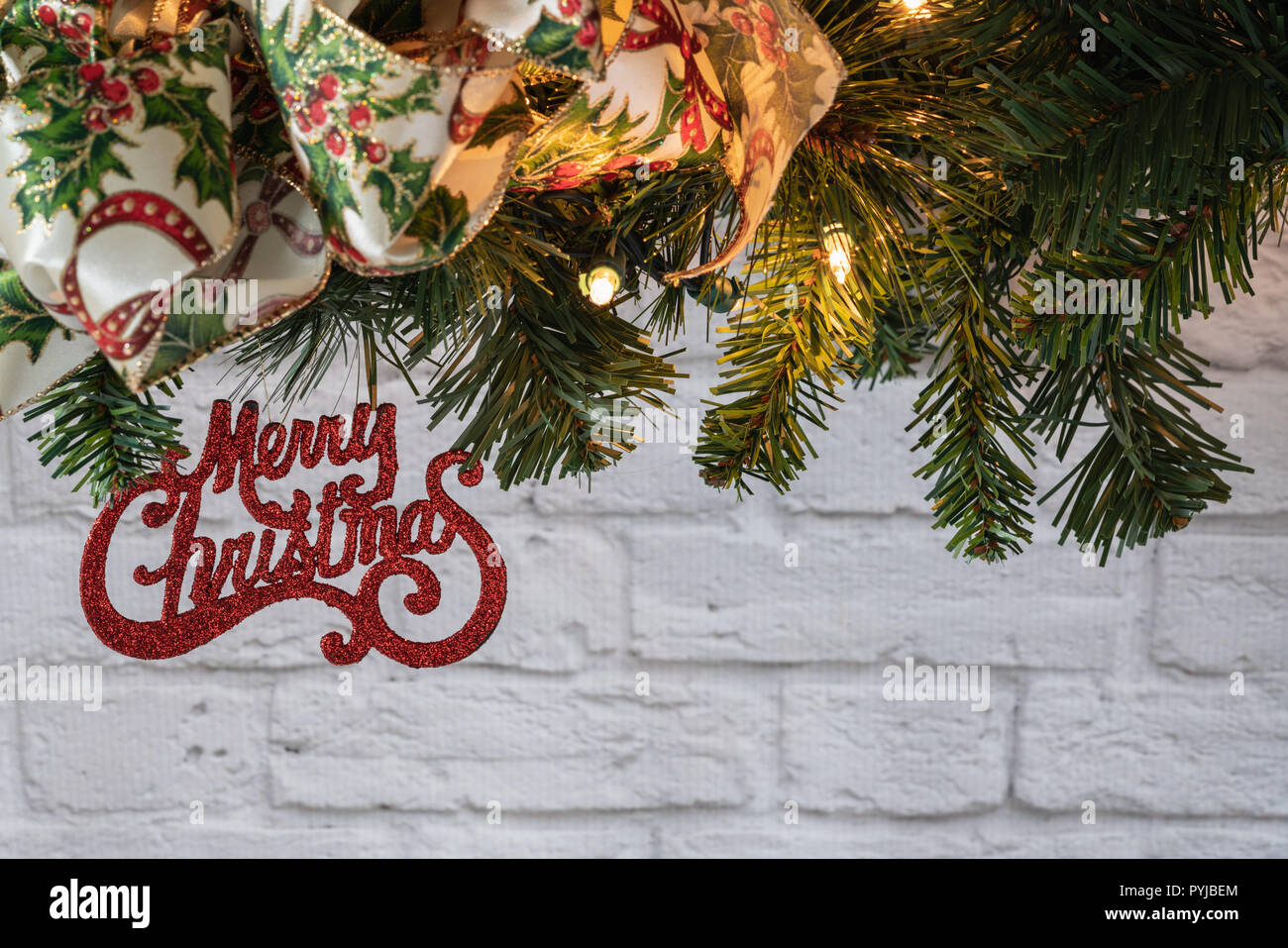 Sur le ruban de verdure avec guirlande joyeux noël ornement en paillettes rouges en face de mur en brique blanche Banque D'Images