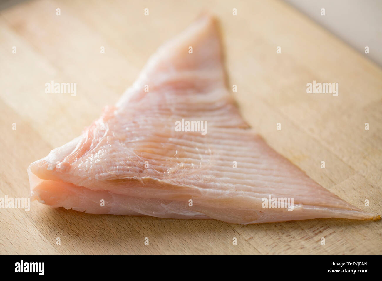 Une section d'une matière première à partir d'une aile ray ray ondulées, Raja undulata, qui a été dépouillé et est prêt pour la cuisson affichée sur une planche à découper en bois. Banque D'Images