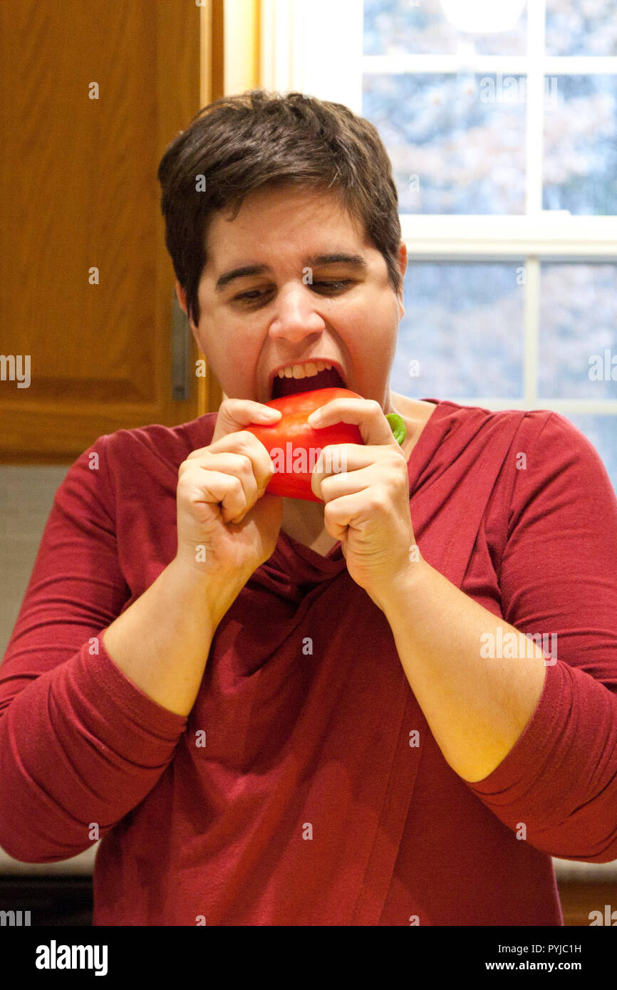 Ouvrant la bouche pour prendre une bouchée d'un poivron rouge dans la cuisine Banque D'Images
