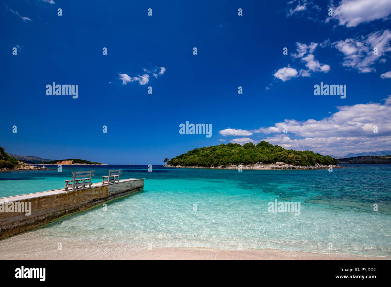 Belle journée de printemps Mer Ionienne avec eau turquoise, sable fin et jetée en bois sur la côte de Ksamil, Albanie. Ciel bleu profond avec des nuages blancs. Banque D'Images