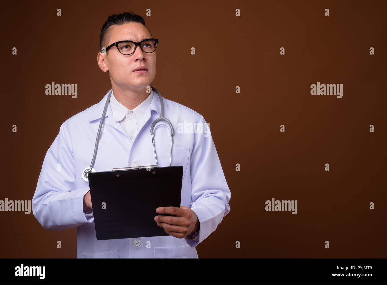 Beau jeune homme multi-ethnique médecin contre fond brun Banque D'Images