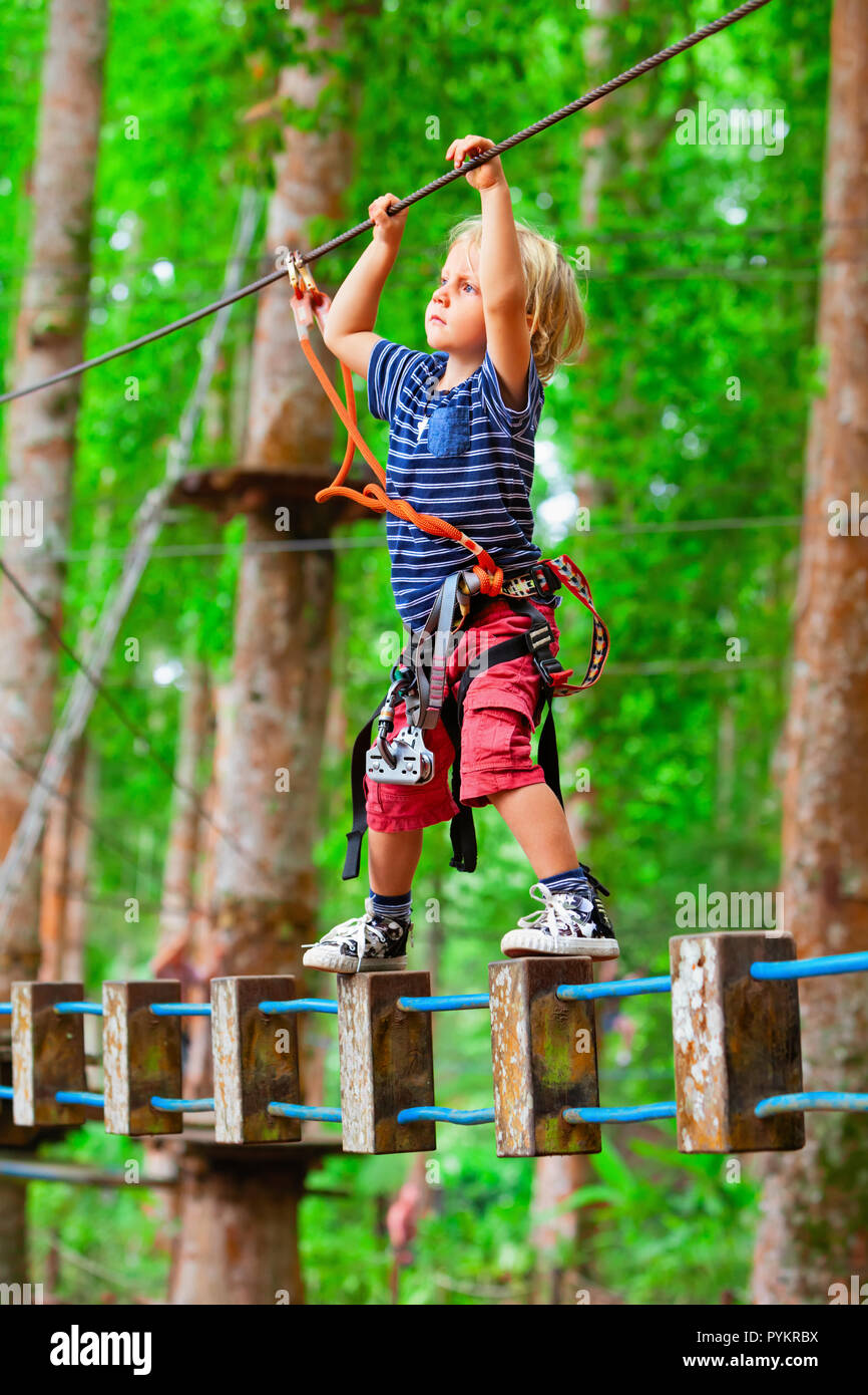 Courageuse jeune enfant dans le harnais de sécurité Grimpez haut sur la cime des arbres, passer pont suspendu obstacle dans l'aventure parc. Activité en plein air. Banque D'Images