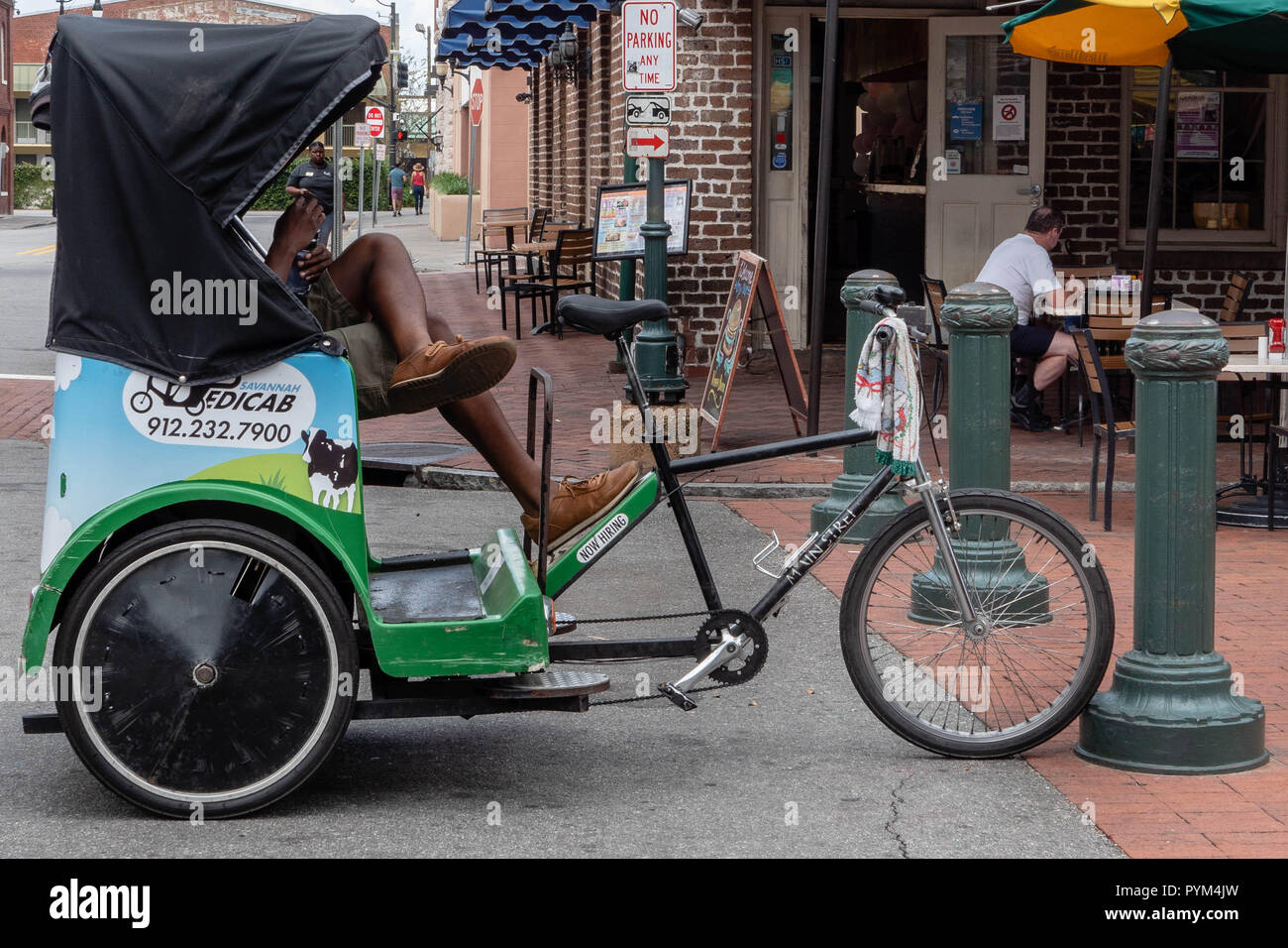 Le conducteur d'un cycle de pousse-pousse ou pedicab taxi en faisant une pause sur un coin de rue à Savannah Georgia USA Banque D'Images