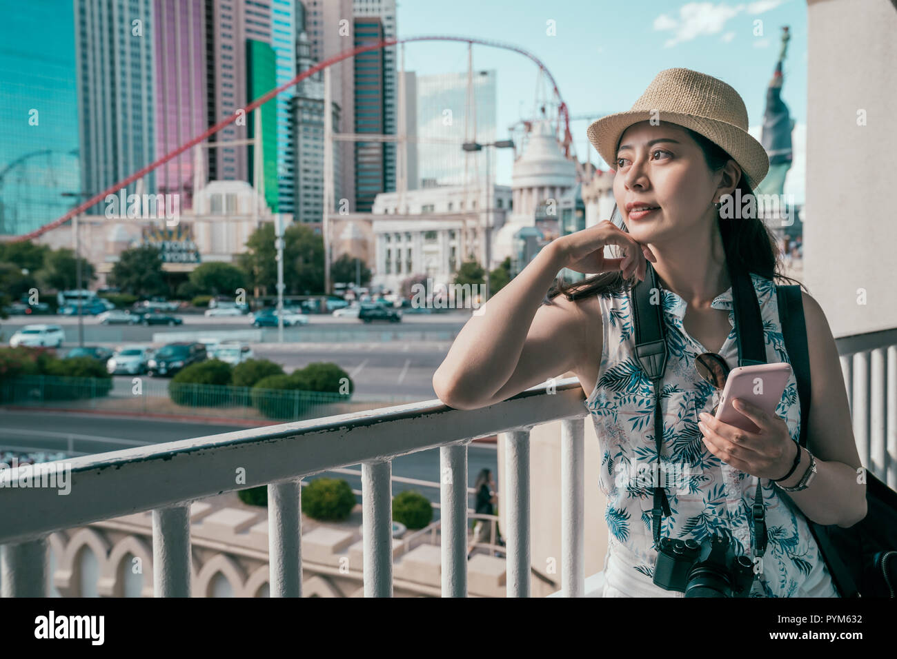 Femme à l'aide de guide touristique en ligne sur téléphone mobile s'appuyant sur la main courante de passage. Profitant de la vue sur la ville en journée ensoleillée. Voyages d'affaires aux États-Unis. Banque D'Images