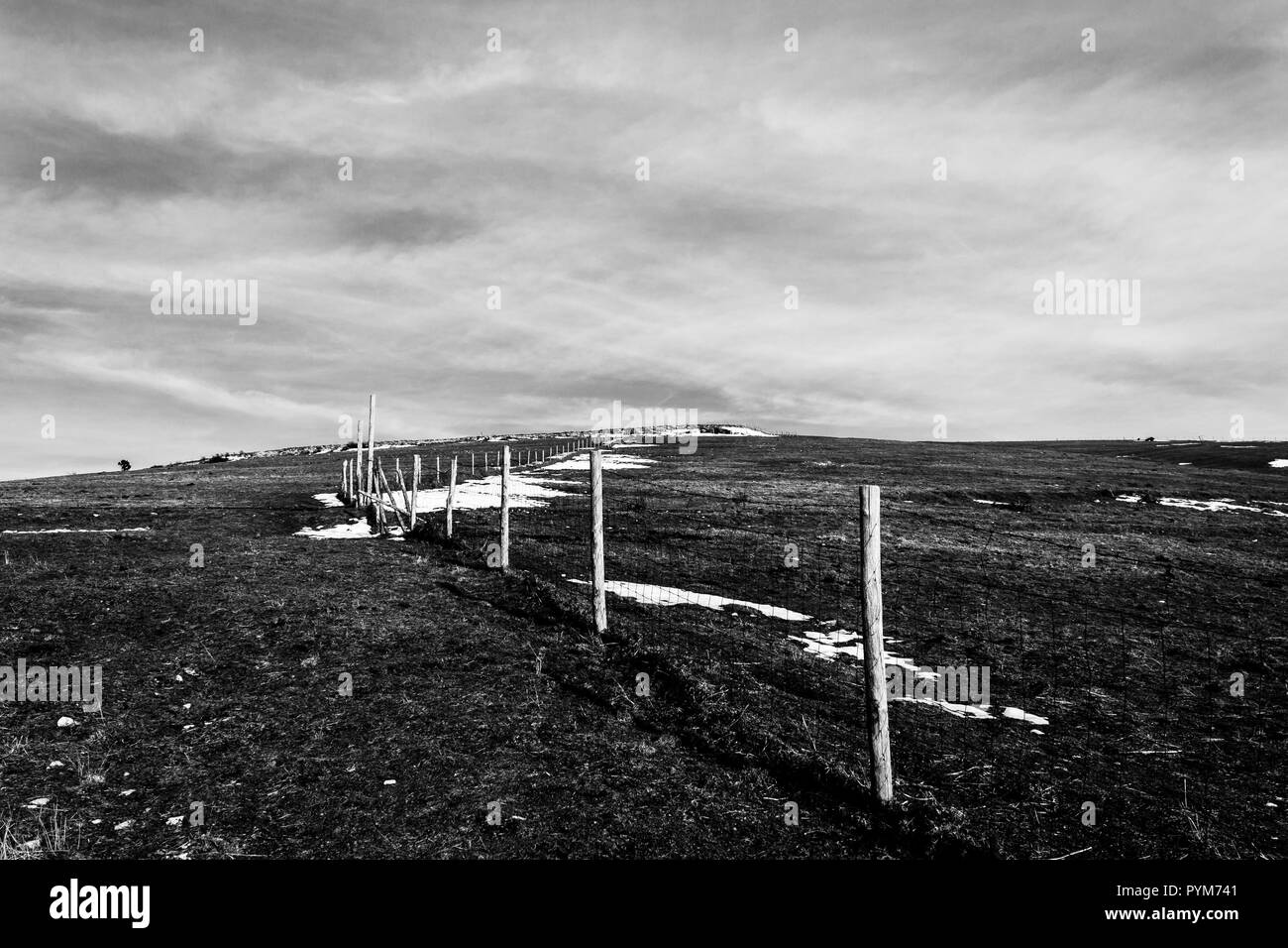 Les poteaux de clôture en bois et des barbelés marquant la limite de la propriété d'une prairie avec des herbes séchées et plaques de neige sous moody sky Banque D'Images