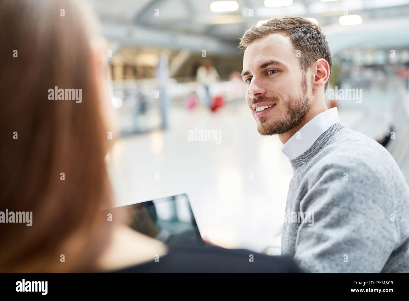 Jeune homme avec un ordinateur portable parlant à une femme dans le terminal de l'aéroport Banque D'Images