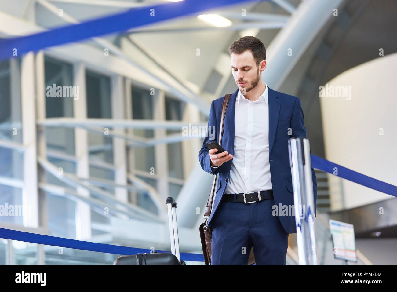 Jeune homme d'affaires en voyage d'affaires porte sur son smartphone en terminal de l'aéroport Banque D'Images