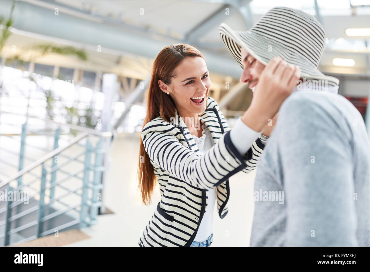 Jeune femme riant de mettre un chapeau d'été sur son partenaire avant de quitter pour les vacances Banque D'Images