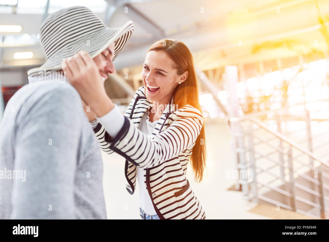Jeune couple de rire à l'aéroport s'amuse avec un chapeau en vacances Banque D'Images