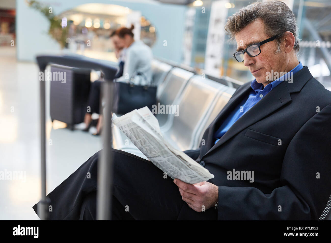 L'homme d'affaires comme un passager se lit journal en zone d'attente de l'aéroport, l'attente pour le vol Banque D'Images