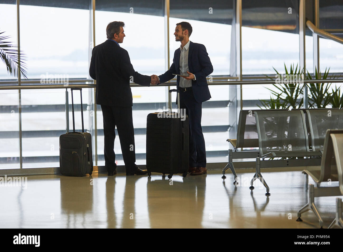 Deux hommes d'affaires en voyage d'affaires à la poignée dans la zone d'attente de l'aéroport Banque D'Images