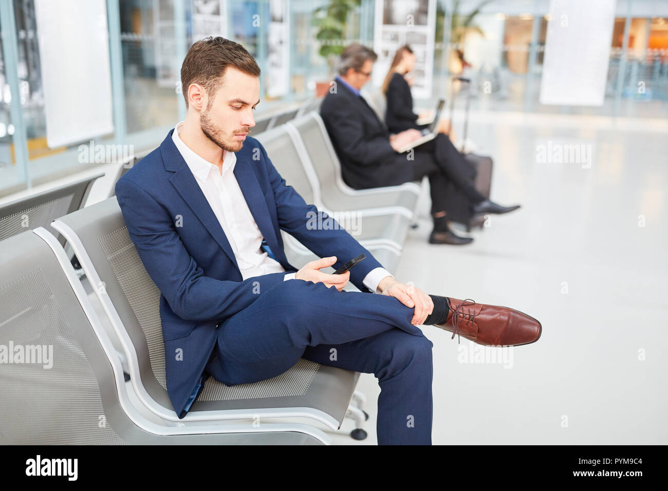 Businessman utilise une application pour smartphone avant son voyage d'affaires dans la zone d'attente de l'aéroport Banque D'Images