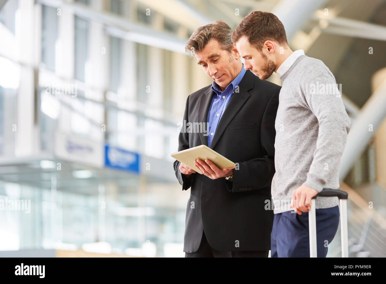 Deux hommes d'affaires à l'aide de tablet dans le terminal de l'aéroport sont à discuter le voyage d'affaires Banque D'Images