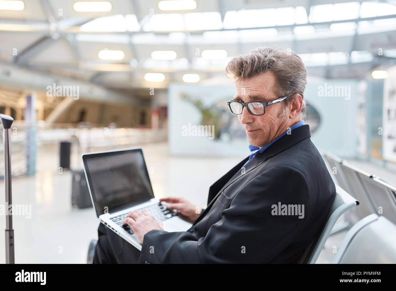 Plein d'assurance manager en voyage d'affaires à taper sur son ordinateur portable dans le terminal de l'aéroport Banque D'Images