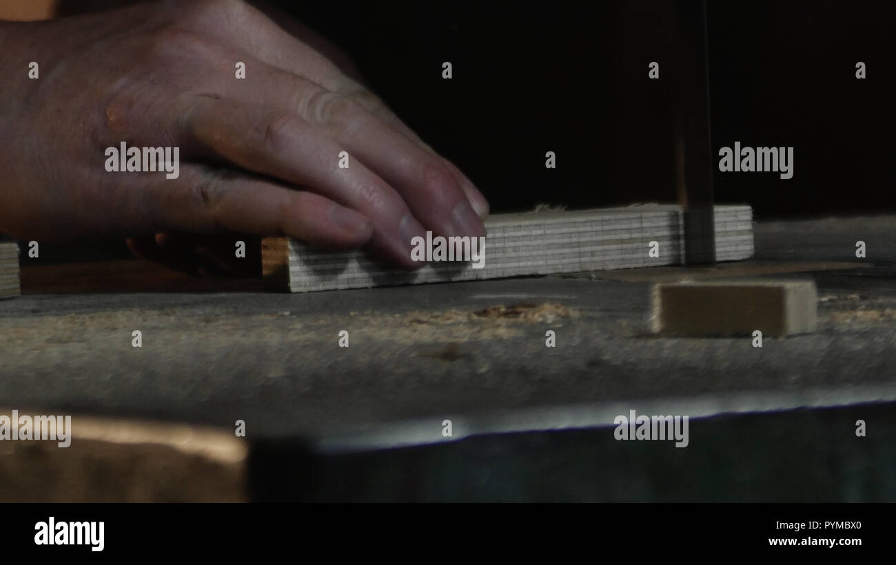 Close up sur les mains de charpentier qui coupe un morceau de bois avec une scie à ruban Banque D'Images