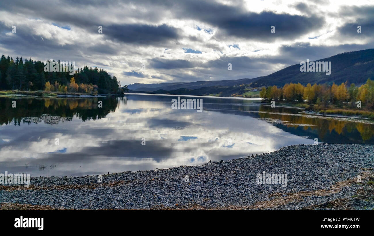 La méditation silencieuse à une plage de galets avec un magnifique cadre rural vue d'un lac tranquille, montagnes, feuillage d'automne et un ciel nuageux. Banque D'Images