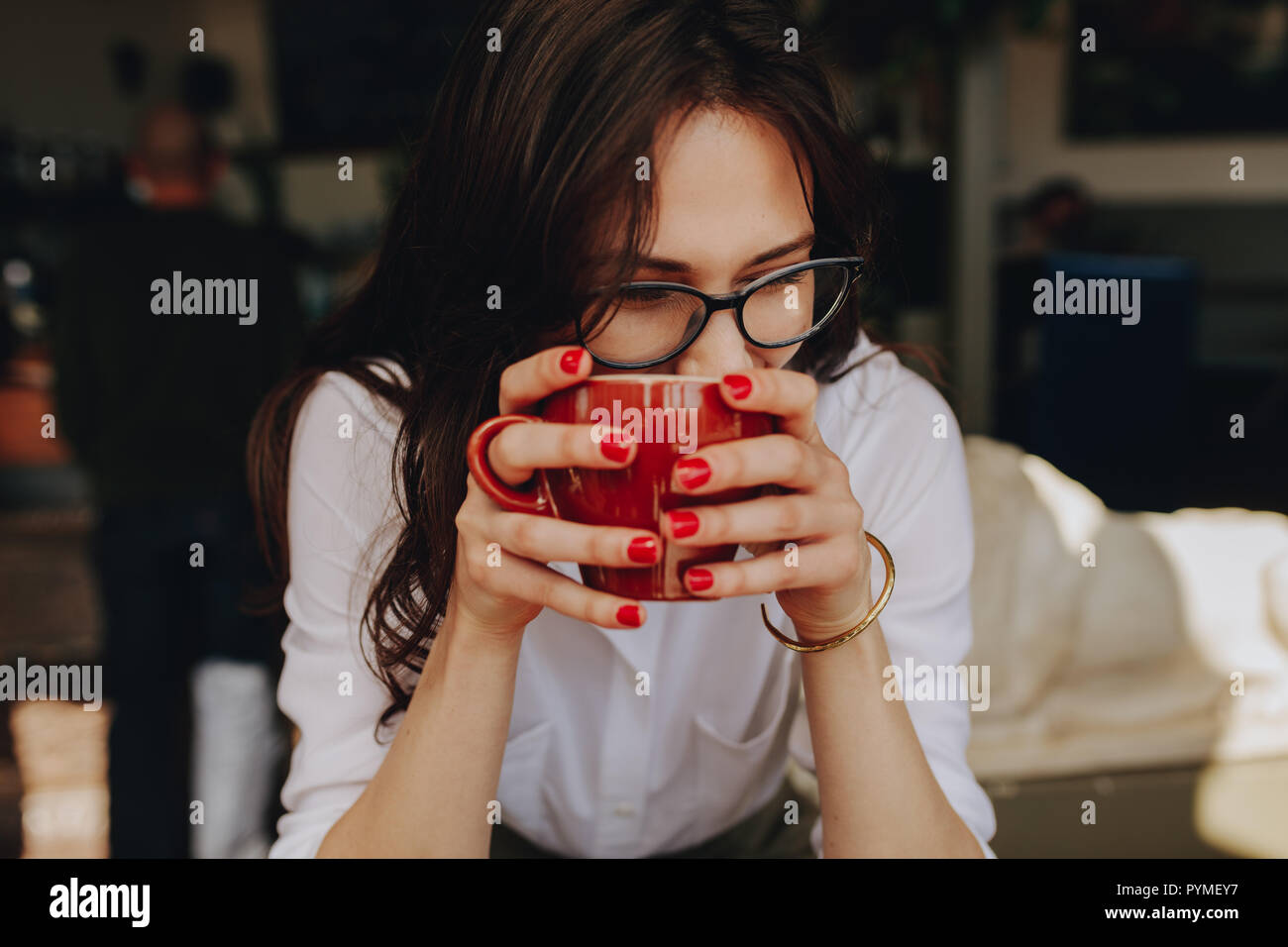 Close up of woman wearing glasses tenant une tasse de café et à la voiture. Femelle avec tasse de café assis au café. Banque D'Images