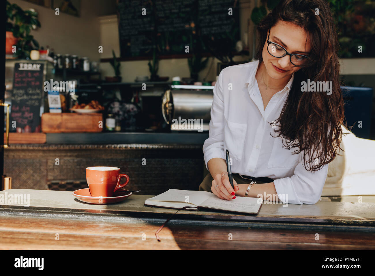 Happy young woman sitting in the cafe à écrire des notes dans son journal. Les femmes prennent des notes dans son livre tout en vous relaxant au coffee shop. Banque D'Images