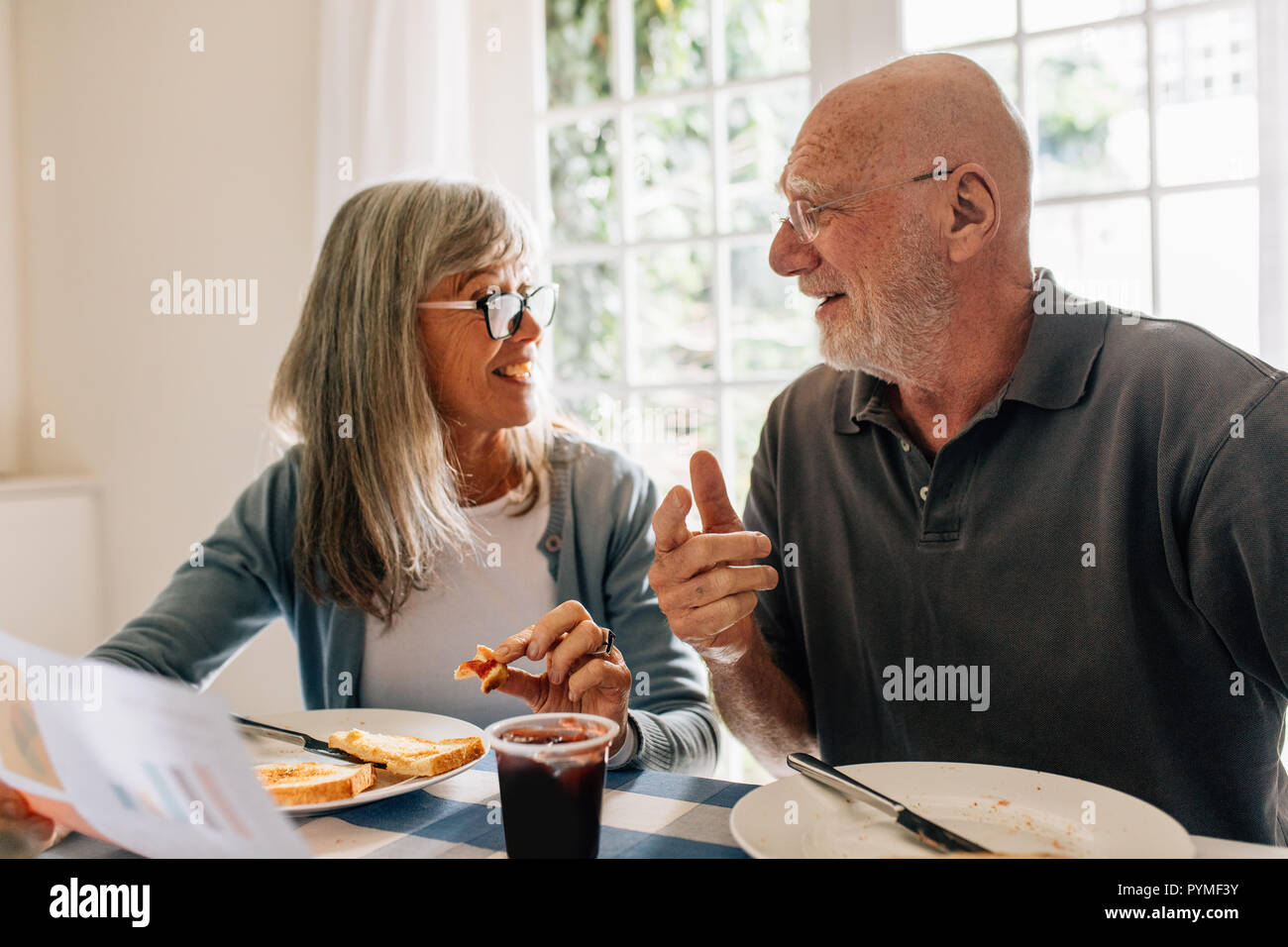 Les cadres supérieurs l'homme et la femme à se parler tout en prenant un petit déjeuner à la maison. Femme tenant un document discutant avec son mari à la table du petit déjeuner. Banque D'Images