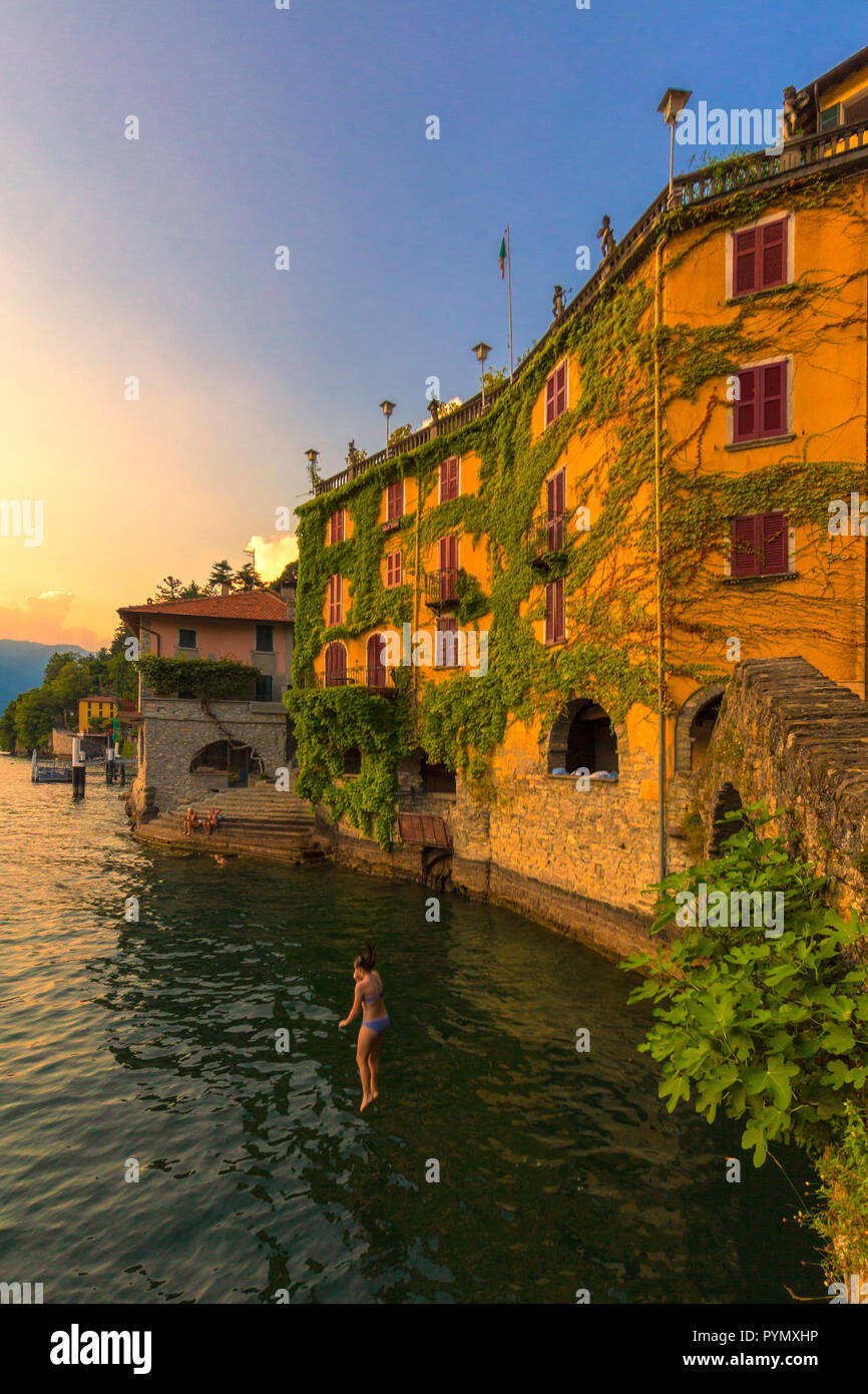 Fille plonge dans le lac depuis un pont au coucher du soleil. Nesso, province de Côme, Lac de Côme, Lombardie, Italie, Europe. Banque D'Images