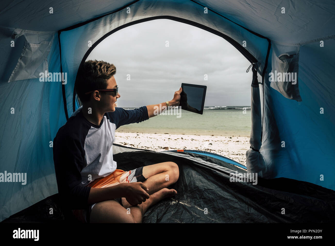 Jeune et beau garçon guy camping directement sur la plage blanche au paradis des îles tropicales. Prendre une photo avec le comprimé sur le livre vert de l'eau Banque D'Images