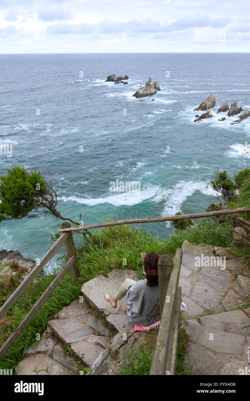 Gueirua beach, Asturias, Espagne. Vue générale de l'observation des femme la mer briser dans le récif était assis sur un vol d'escaliers en pierre. Banque D'Images