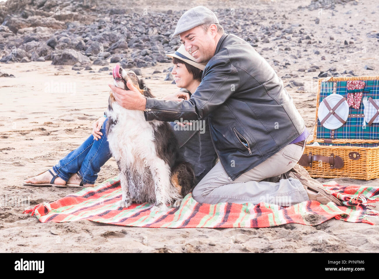 Couple dans l'amour et de partenariat à la plage au cours d'un pique-nique avec meilleur ami chien avec eux dans l'activité ludique. Le bonheur et la zoothérapie pour profiter de FRV Banque D'Images