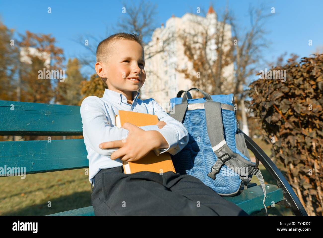 Petit garçon 6, 7 ans avec un livre. Portrait d'un enfant avec le grand livre, la lecture et assis sur un banc. Banque D'Images