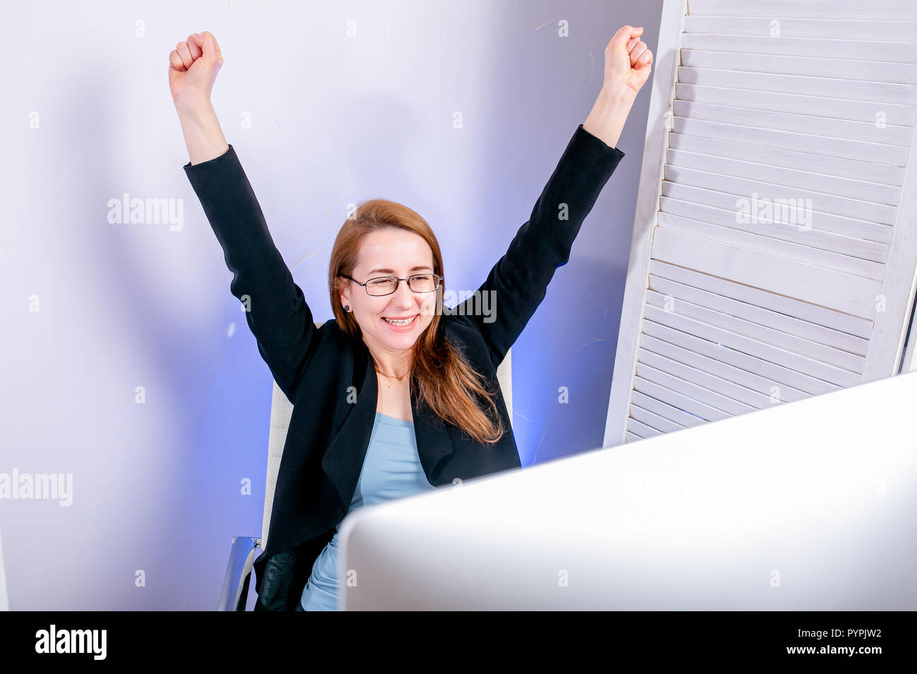 Portrait of happy young businesswoman réussie fêter quelque chose avec les bras jusqu'au bureau. Les émotions positives. Big Deal, promotion, gagner la loterie ou dis Banque D'Images