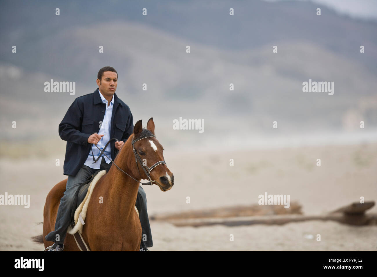 Mid-adult man riding un cheval brun le long d'une plage éloignée. Banque D'Images