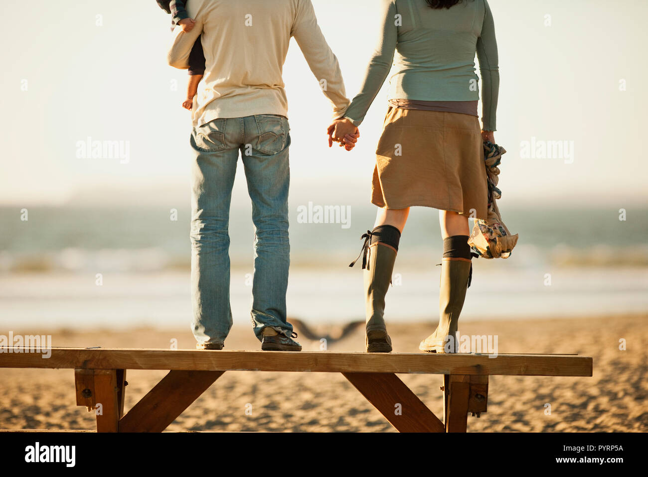 Jeune Couple Avec Bebe Tenir La Main Tout En Se Tenant Debout Sur Un Banc En Bois Face A La Mer Photo Stock Alamy