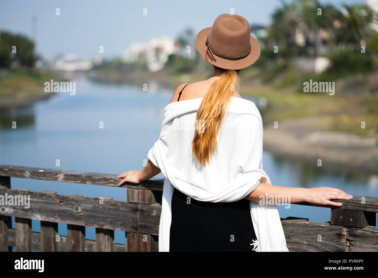 Modèle féminin pose par l'eau avec un chapeau brun, robe noire et blanche est Banque D'Images