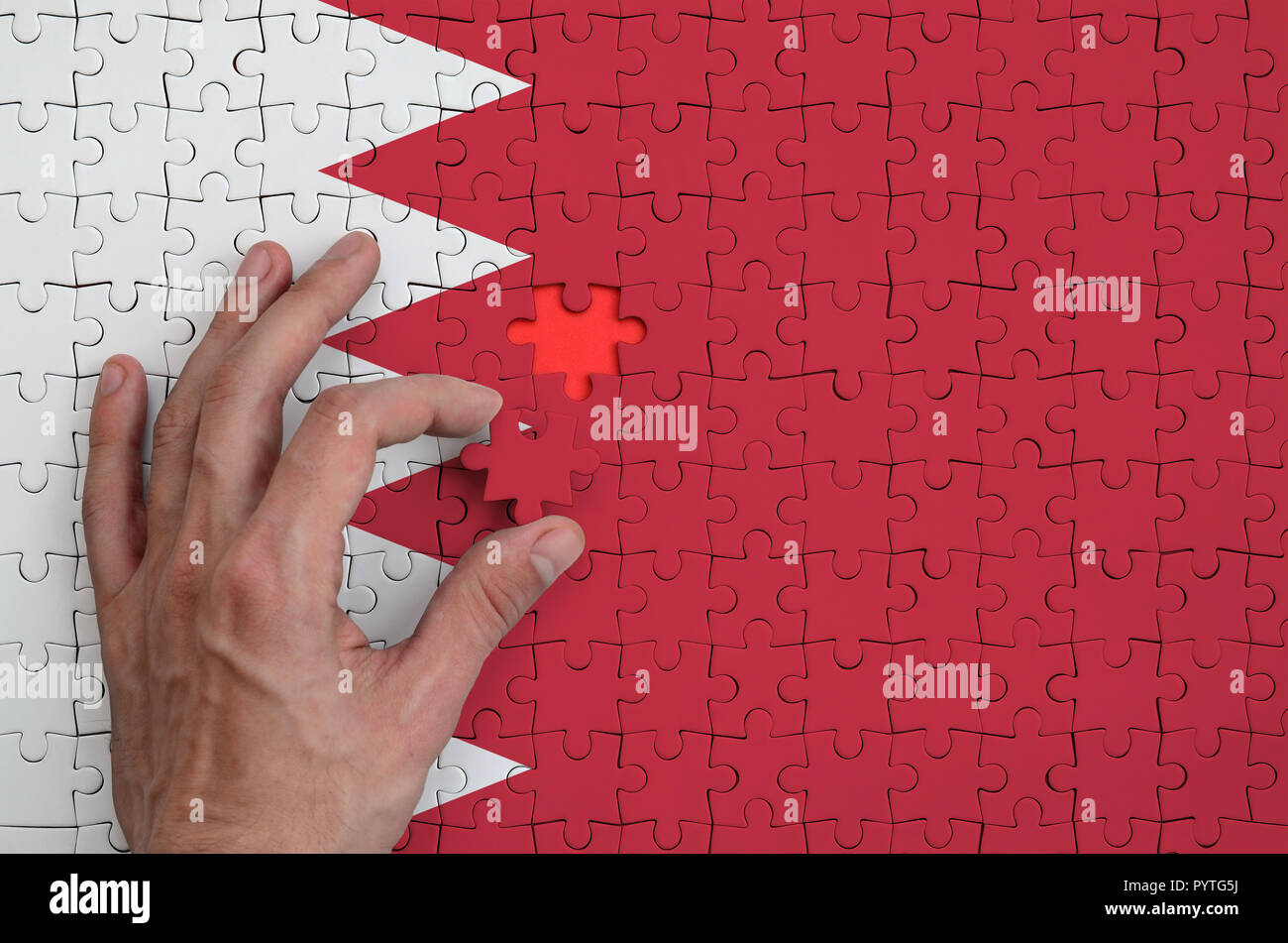 Drapeau de Bahreïn est représenté sur un casse-tête, qui la main de l'homme achève de se plier. Banque D'Images
