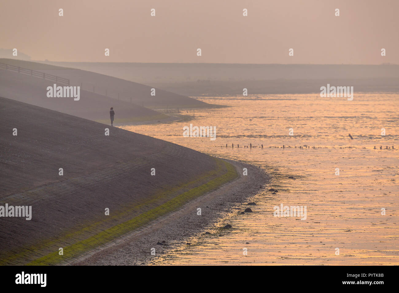 Personne regardant le coucher du soleil de Delta fonctionne de la digue la mer de Wadden en orange haze autour de coucher du soleil à Friesland, Pays-Bas Banque D'Images