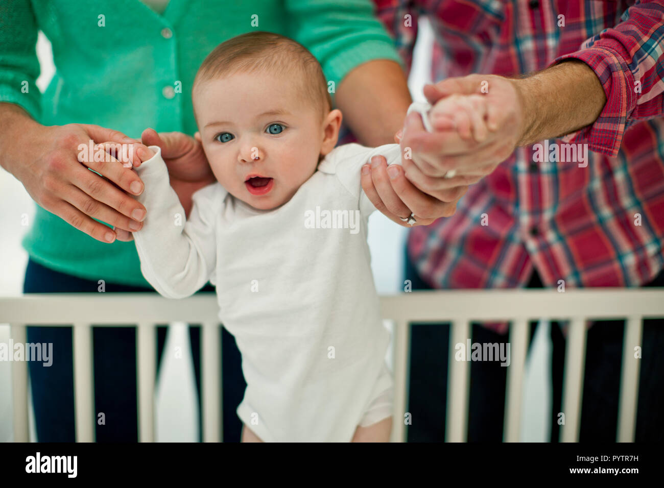 Cute smiling Baby Boy est pris en charge par les mains de ses parents comme ils l'aider à rester dans son lit pour la première fois. Banque D'Images