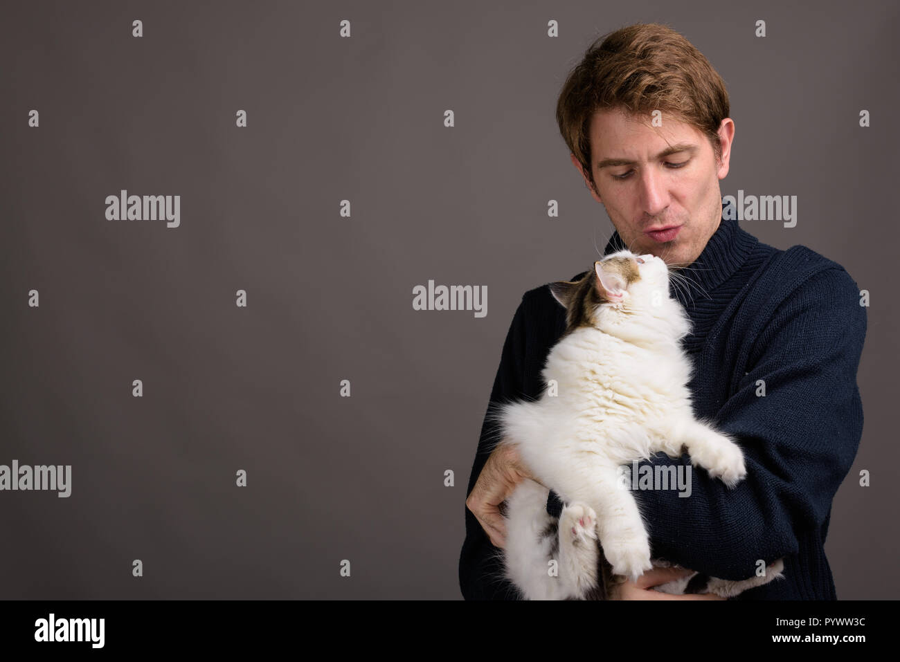 Handsome man holding Cute cat contre l'arrière-plan gris Banque D'Images