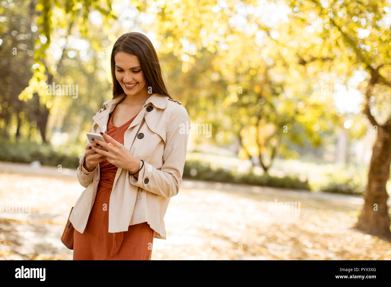 Happy young woman using cell phone in autumn park sur belle journée Banque D'Images