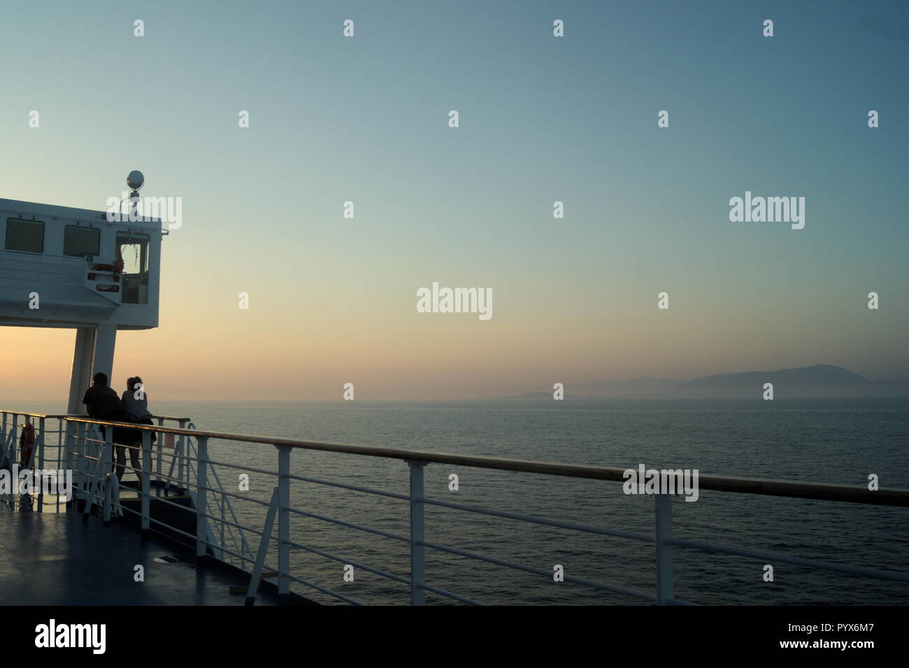 Coucher de soleil depuis le pont d'un ferry inter-île en traversant la mer Égée en Grèce. Deux passagers regardent le soleil se coucher. Copier l'espace. Banque D'Images