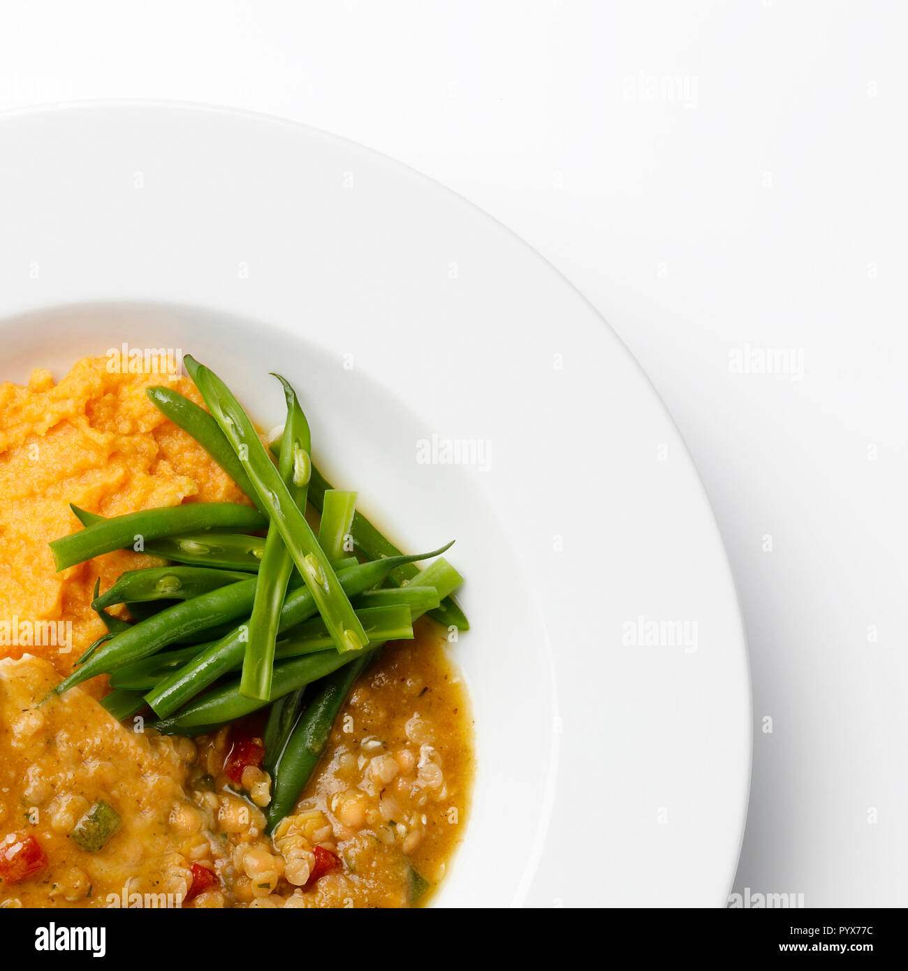 Coin d'une plaque blanche avec des haricots verts, une sause de lentilles et de la purée de patate douce, sur fond blanc. Banque D'Images