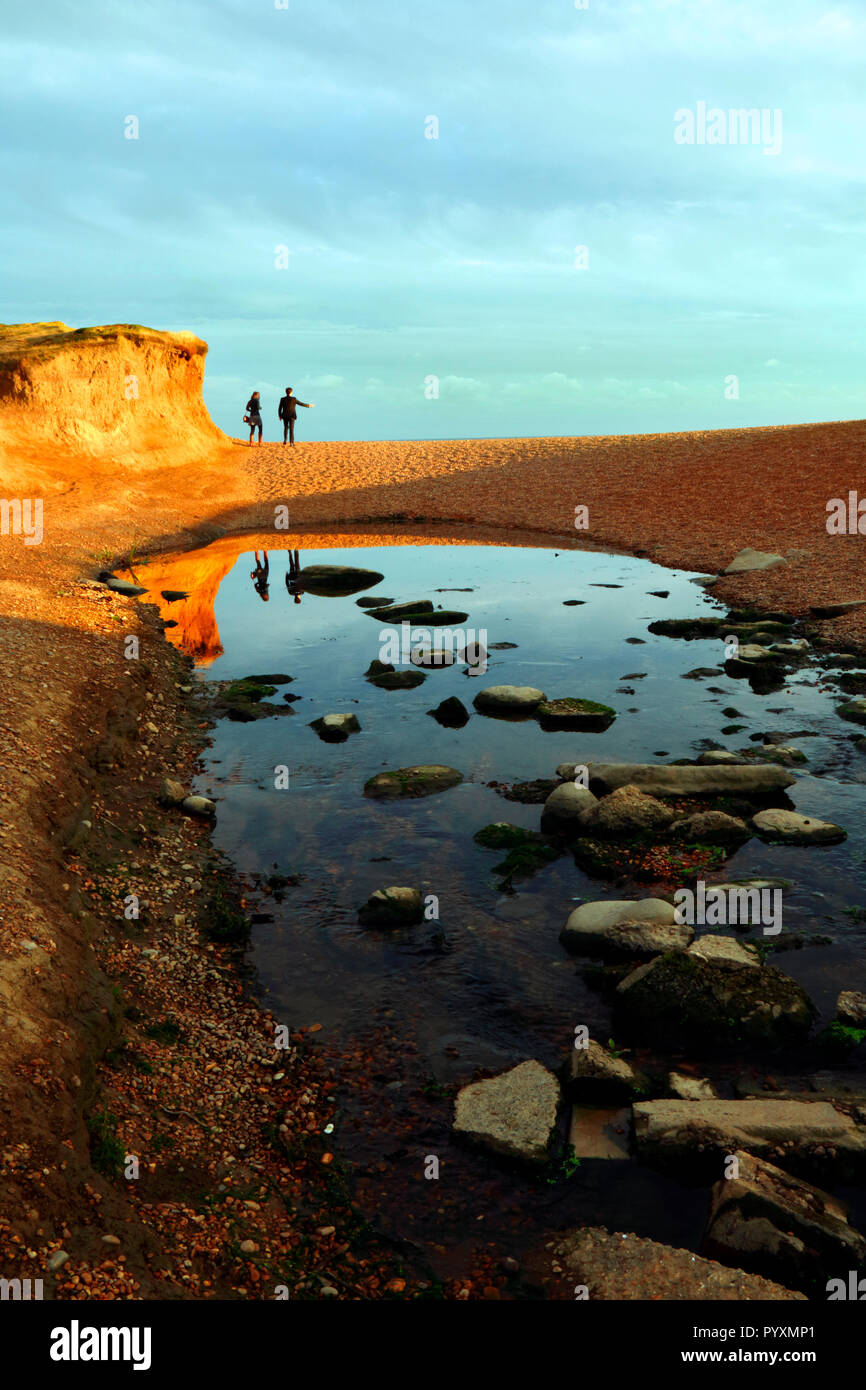 Un couple en train de marcher sur la plage de Seatown dans Dorset près de au coucher du soleil avec des réflexions dans un ruisseau Banque D'Images