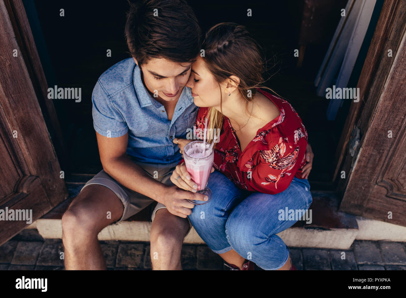Couple d'humeur romantique assis ensemble le partage d'un milkshake. Femme posant sa tête sur l'épaule de son homme. Banque D'Images