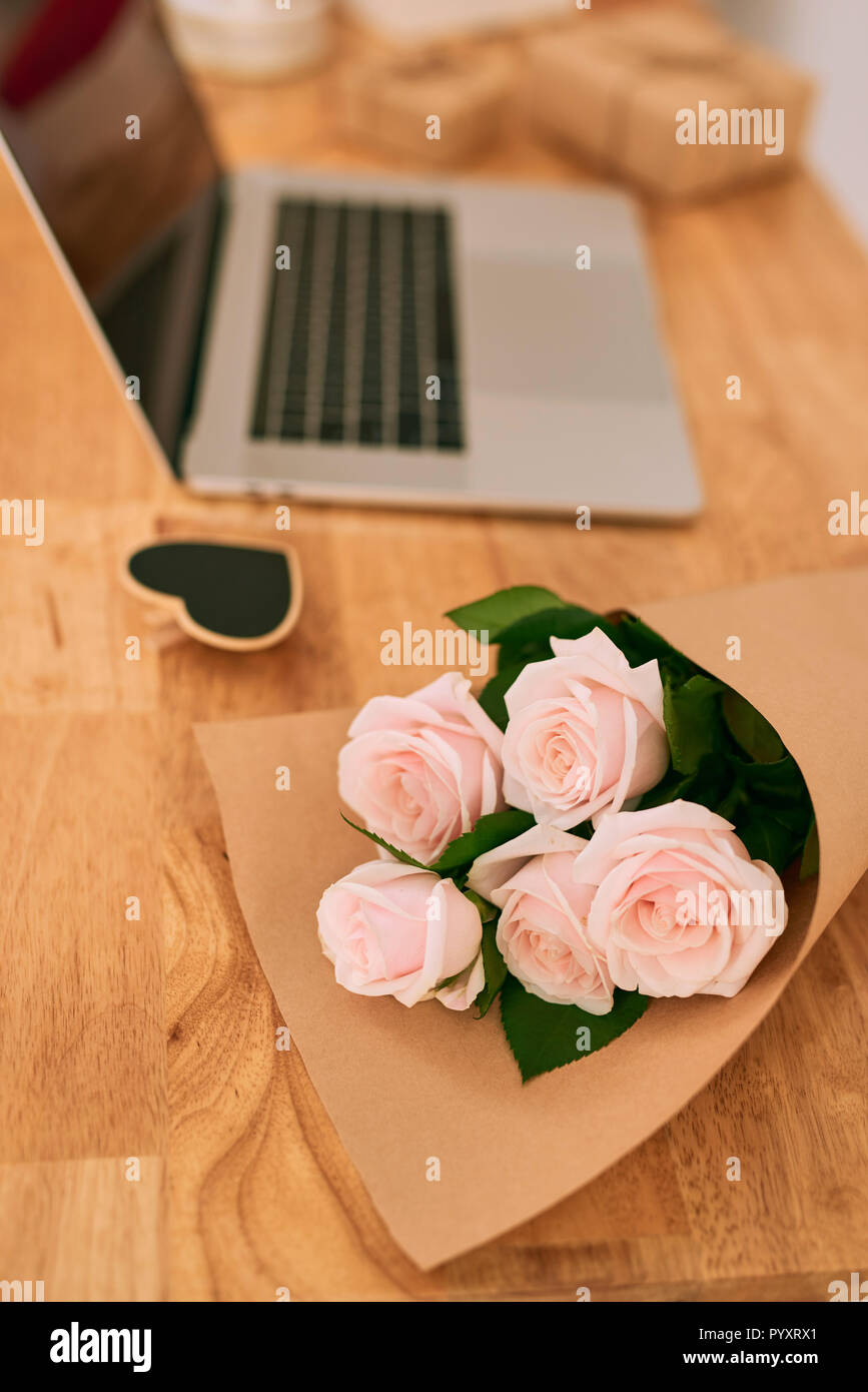 Roses roses sur la table en bois avec ordinateur portable. Banque D'Images