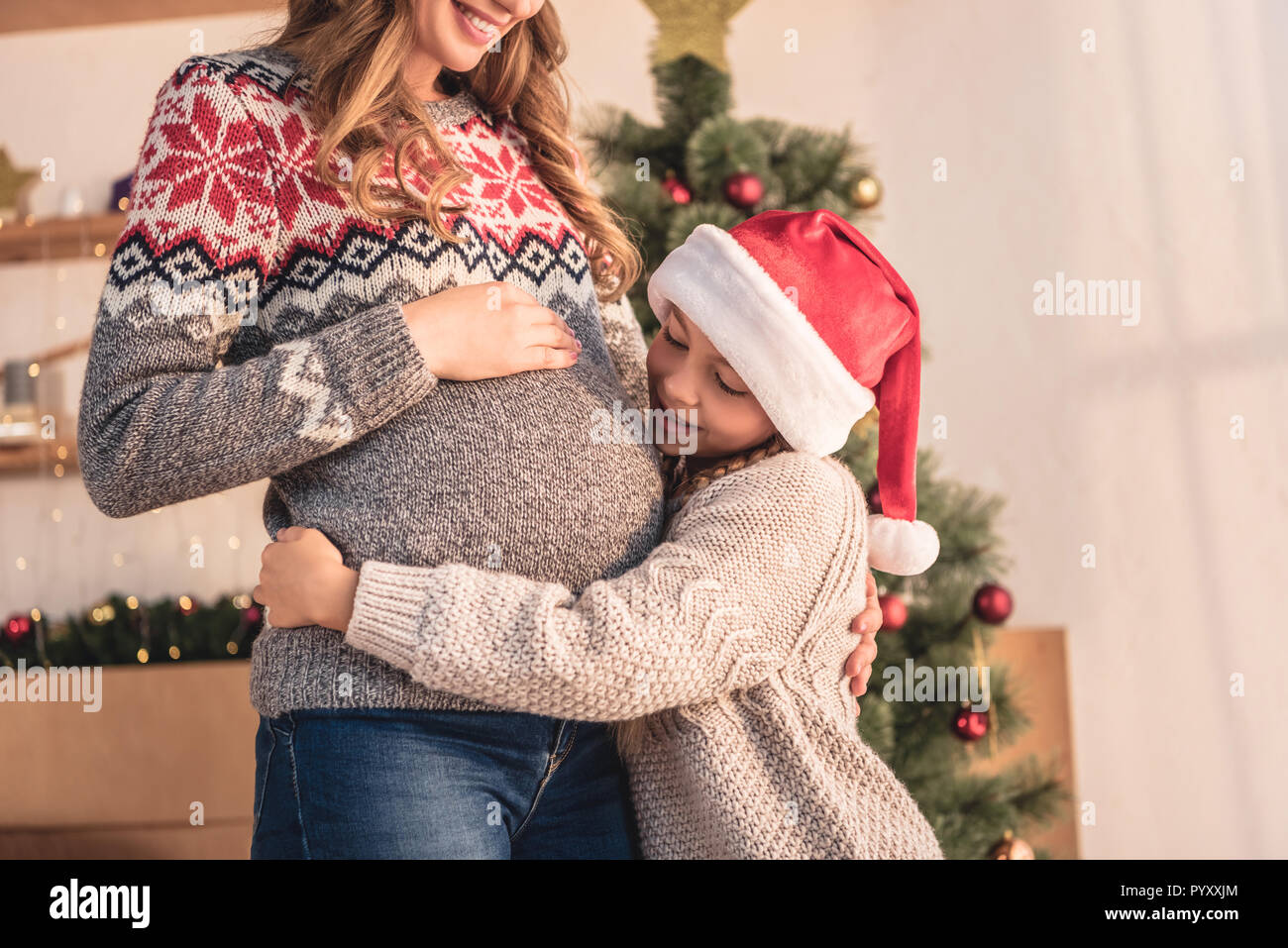 Portrait de fille à santa hat hugging mère enceinte près de l'arbre de Noël à la maison Banque D'Images