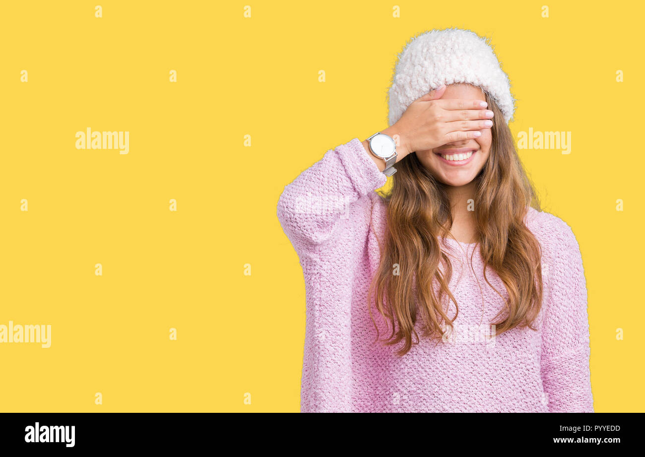 Jeune belle brunette woman wearing sweater et chapeau d'hiver sur fond isolé sourire et rire avec la main sur le visage pour les yeux couvrant surpri Banque D'Images