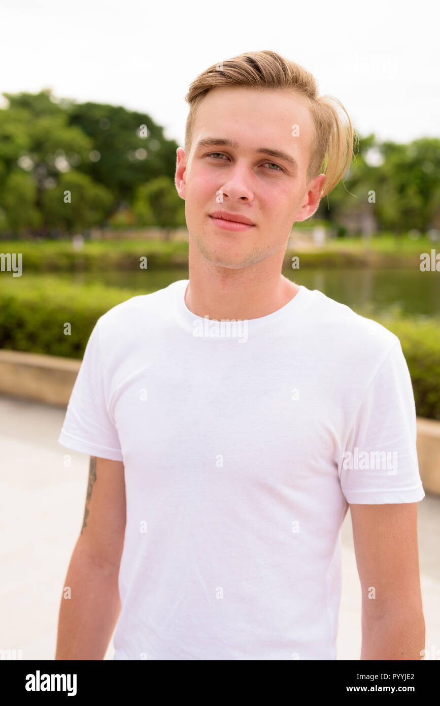 Beau jeune homme aux cheveux blonds se détendre dans le parc Banque D'Images