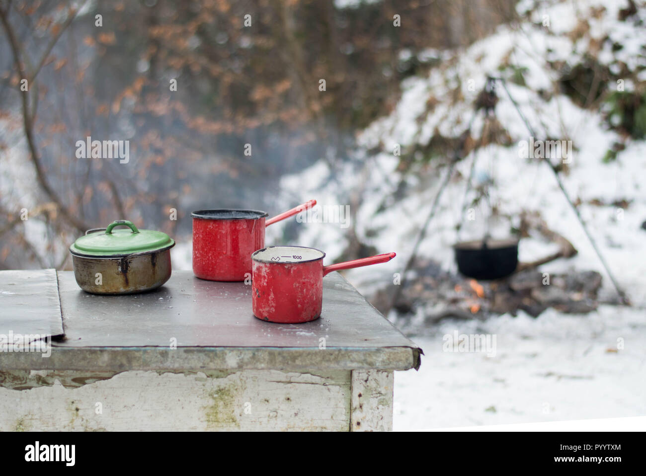 Plats d'émail sur la table - cuisine en plein air en hiver par feu de camp dans la forêt Banque D'Images