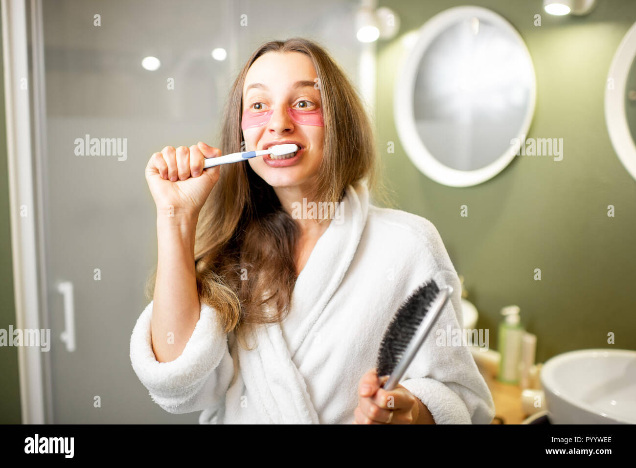 Jeune et belle femme en peignoir se brosser les dents dans la salle de bains Banque D'Images