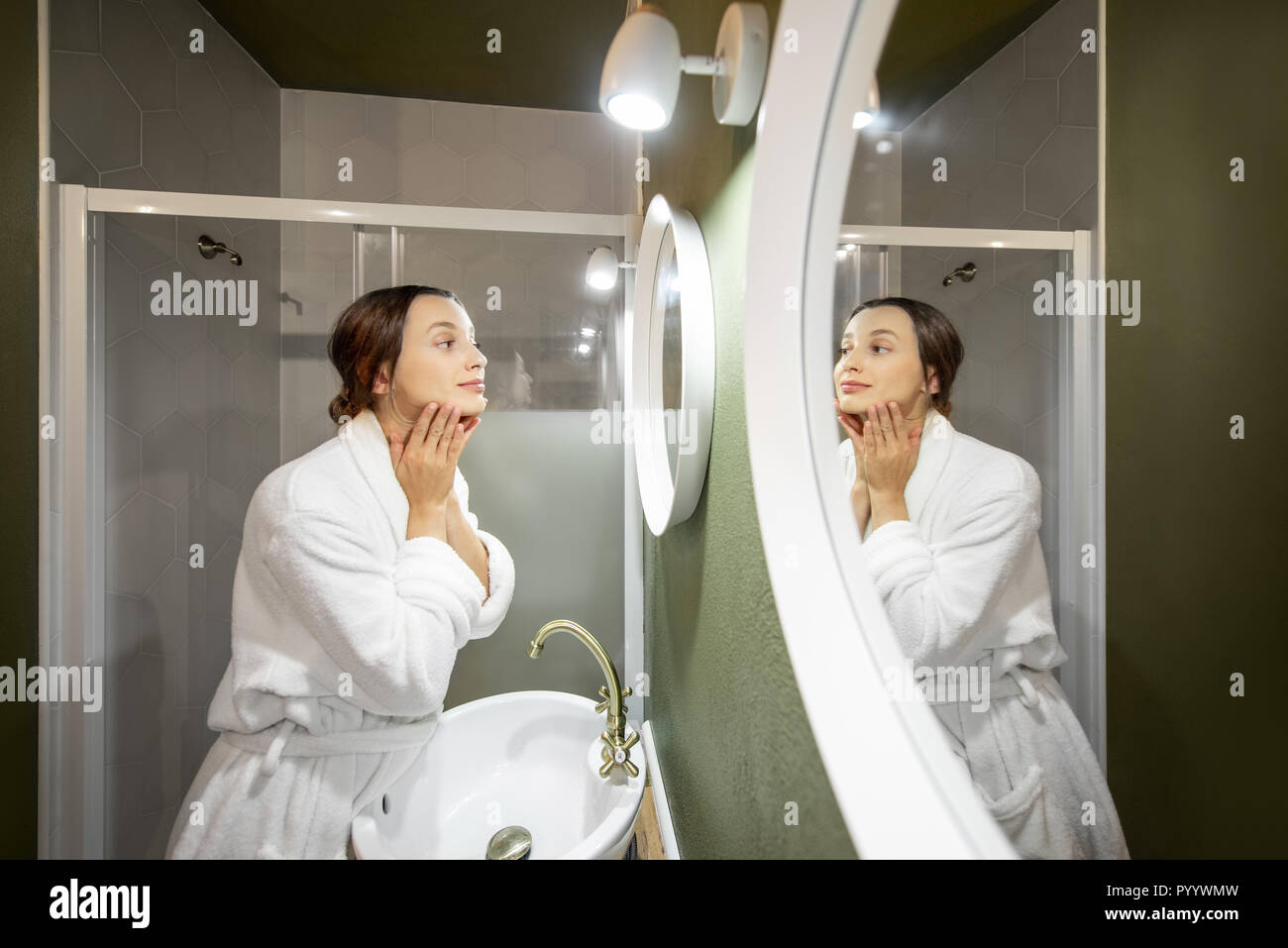 Femme en peignoir faire massage du visage à la ronde dans le miroir dans la salle de bains Banque D'Images