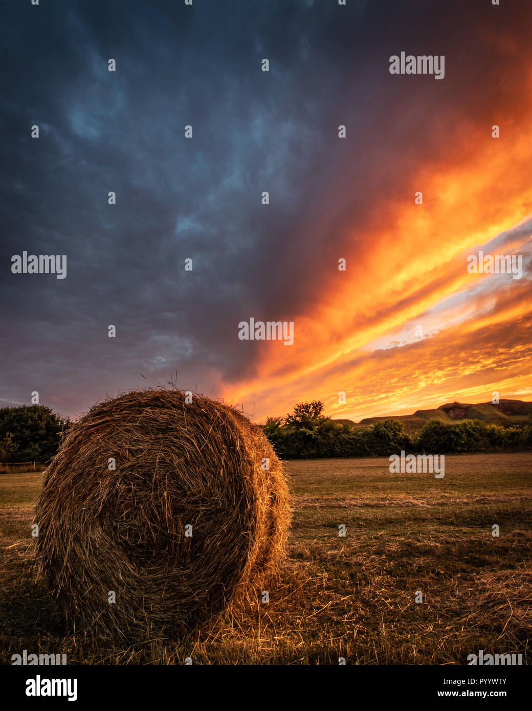 Un seul balles de foin dans un champ au coucher du soleil avec les nuages de tempête divisant le coucher du soleil dans un champ de Hampshire Banque D'Images