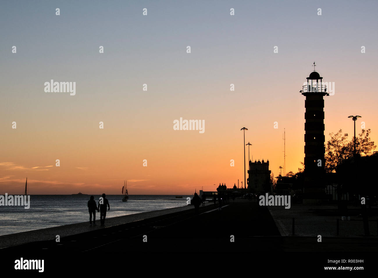 Coucher du soleil sur le Tage (Rio Tejo) avec phare et la Tour de Belém (Torre de Belem) dans le quartier de Belém, Lisbonne, Portugal. Banque D'Images